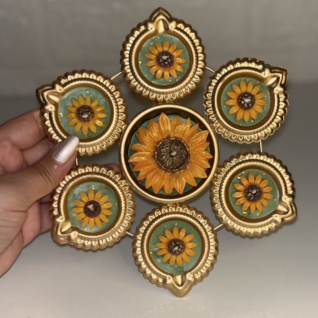 DH-04: Six sunflower diyas around one big sunflower, joined in a gold metal frame, held in a hand, to show its size.