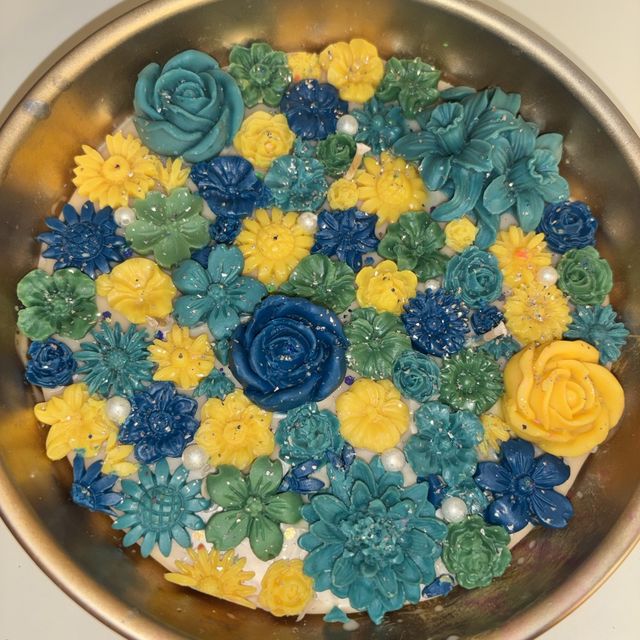 DH-05: An antique-gold metal urli full of blue, teal and yellow flowers, close-up of the flowers.